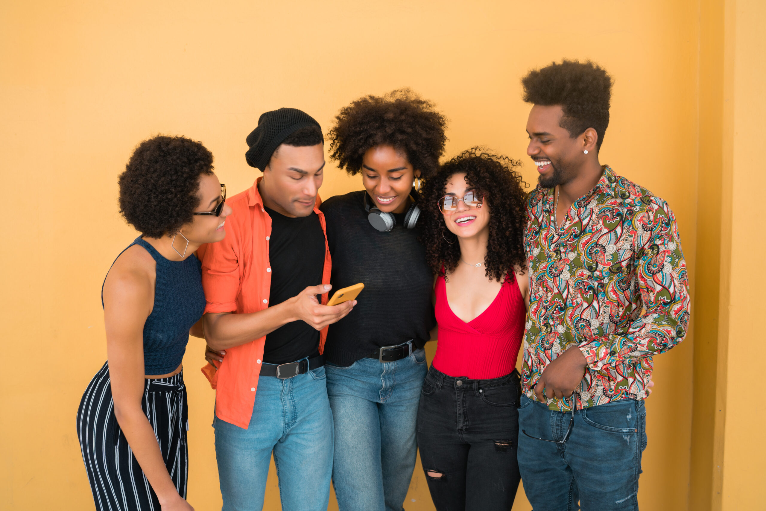 Revealed: The Surprising Divide Between Nigerian Millennials and Gen Z 12 A joyful group of young Nigerian friends — representing Millennials and Gen Z — laughing and bonding together against a bright yellow wall as they happily view something on a smartphone.