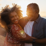 Smiling middle-aged couple embracing on a beach at sunset, sharing a warm and joyful moment that reflects trust, love, and emotional connection.