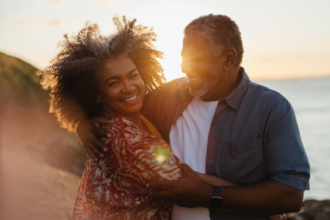 Smiling middle-aged couple embracing on a beach at sunset, sharing a warm and joyful moment that reflects trust, love, and emotional connection.