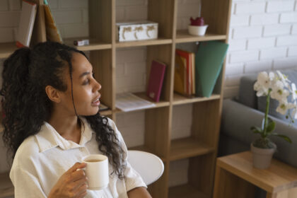 Young professional working from home on a laptop while reviewing financial charts and documents, holding a cup of coffee at a modern home office desk.