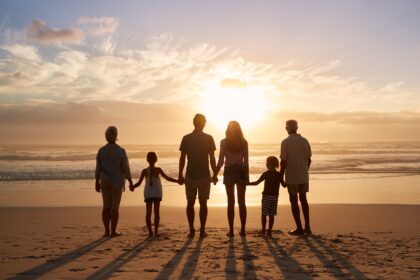 Family of four walking along a sunny beach, holding hands and enjoying quality time together during a fun seaside vacation.