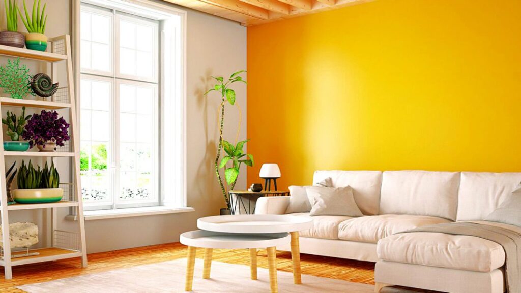 The Perfect Paint Colours for Your Home: Beating Humidity, Heat and Looking Beautiful 11 Modern living room with a bright yellow accent wall, white sofa, indoor plants, and large windows showcasing stylish interior paint ideas.