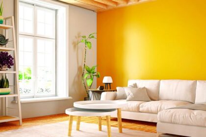Modern living room with a bright yellow accent wall, white sofa, indoor plants, and large windows showcasing stylish interior paint ideas.
