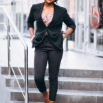 Young professional woman wearing a black blazer and tailored trousers with red heels, walking confidently down office steps in a stylish corporate outfit.