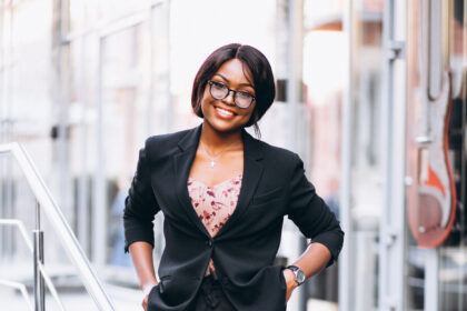 Young professional woman wearing a black blazer and tailored trousers with red heels, walking confidently down office steps in a stylish corporate outfit.