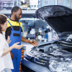 Mechanic explaining engine maintenance to a car owner during a vehicle inspection at an auto repair workshop.