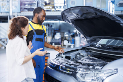 Mechanic explaining engine maintenance to a car owner during a vehicle inspection at an auto repair workshop.
