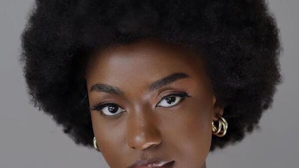Woman with natural afro hair posing for a portrait against a grey background.