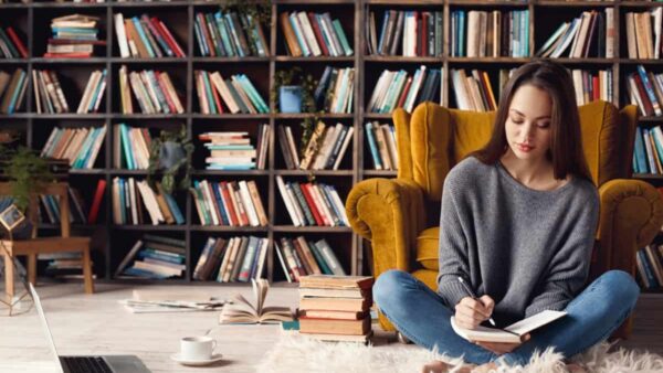 Woman holding a book and standing in front of a home bookshelf.