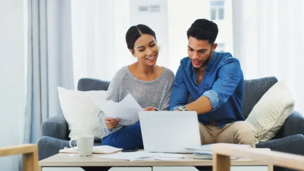 Couple sitting together at home, discussing finances and reviewing documents on a laptop.