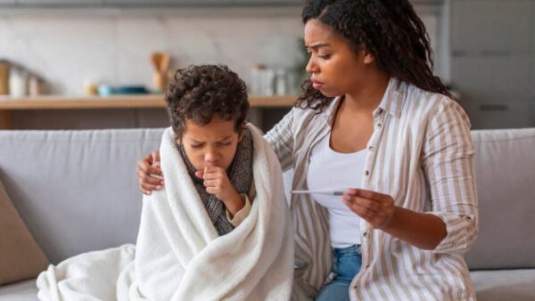 Nigerian mother caring for a sick child at home while checking their temperature.