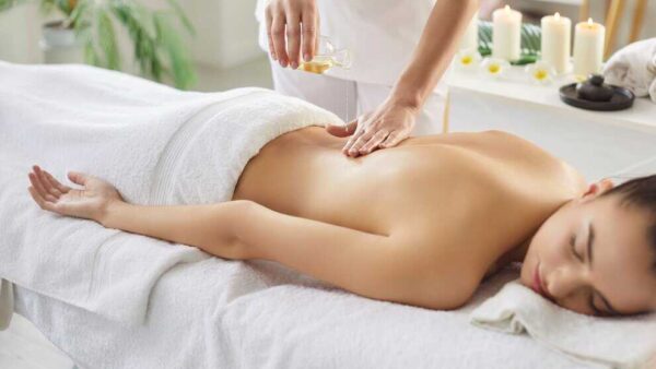 Therapist applying warm oil to a woman’s back during a relaxing body massage at a spa.